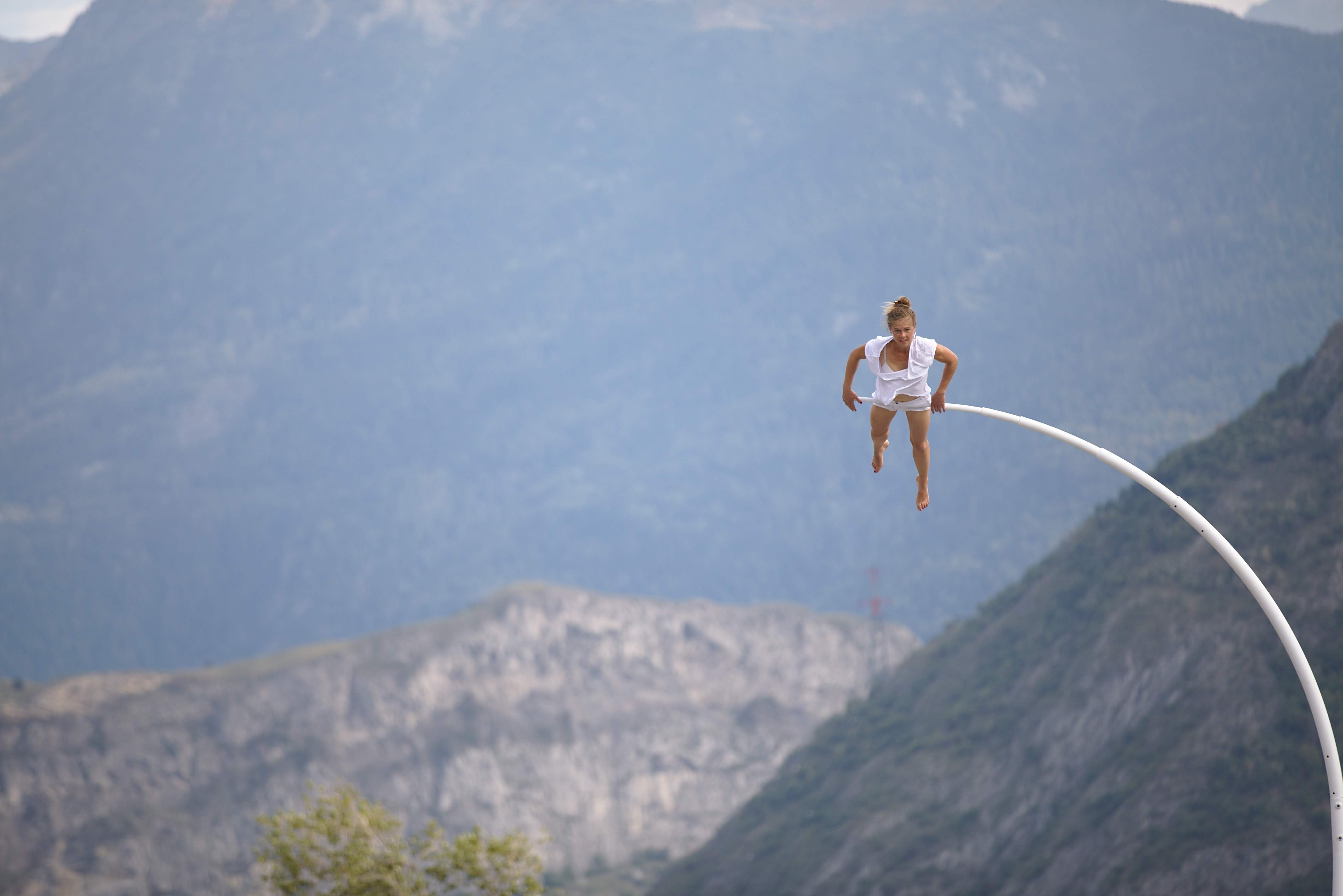 Chloé Moglia suspended horizontally beneath a curved steel bar against the sky