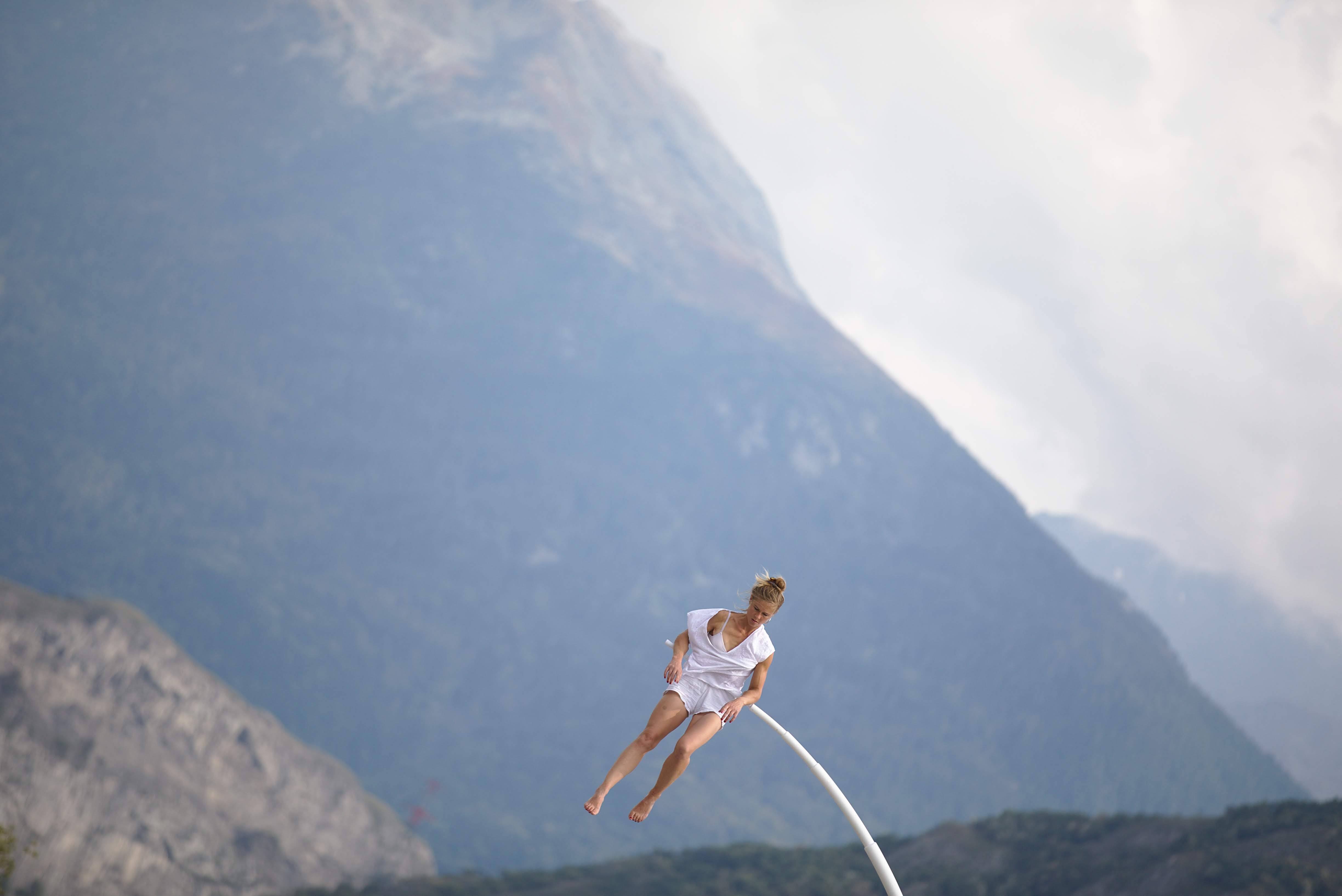 Chloé Moglia balancing and hanging across a curved aerial apparatus above an outdoor audience