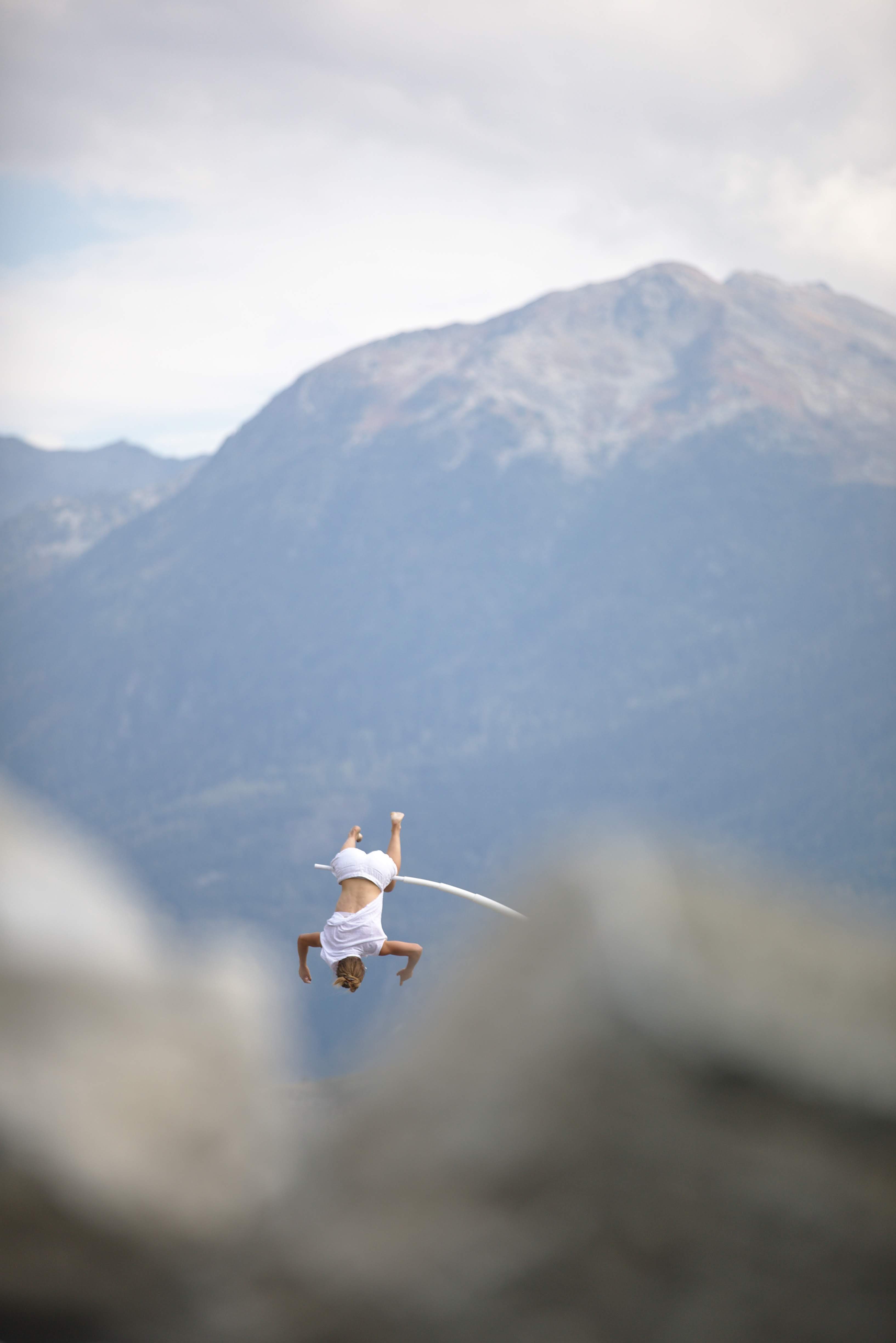 Chloé Moglia hanging vertically from a high curved metal apparatus during an outdoor suspension performance
