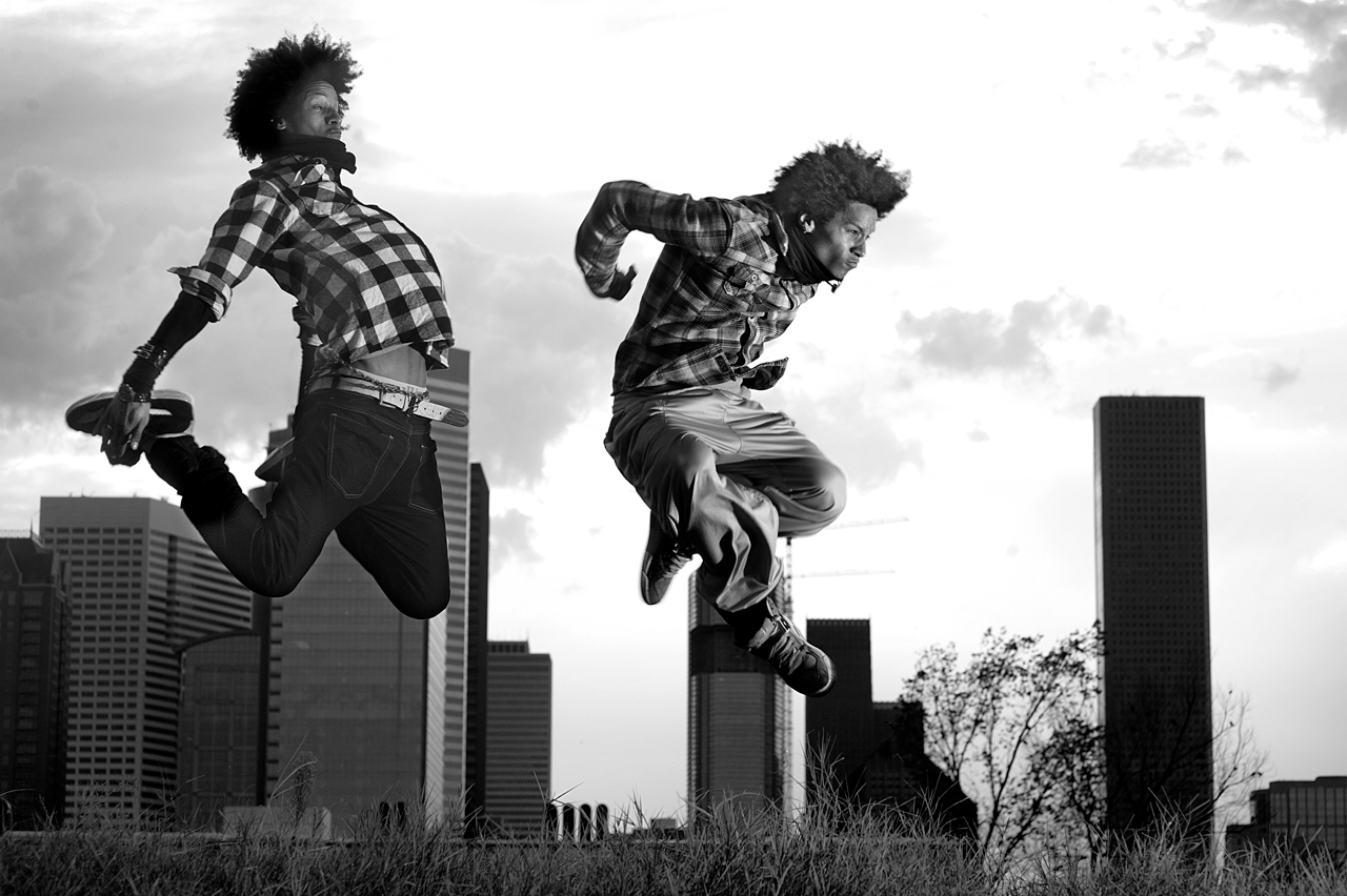 Black-and-white photograph of Les Twins jumping against a city skyline