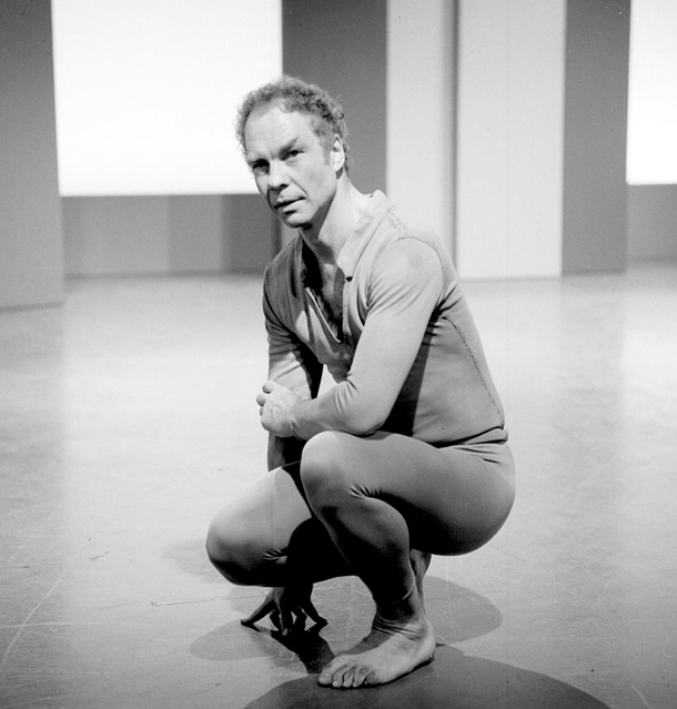 Merce Cunningham crouching on a stage in dance clothing