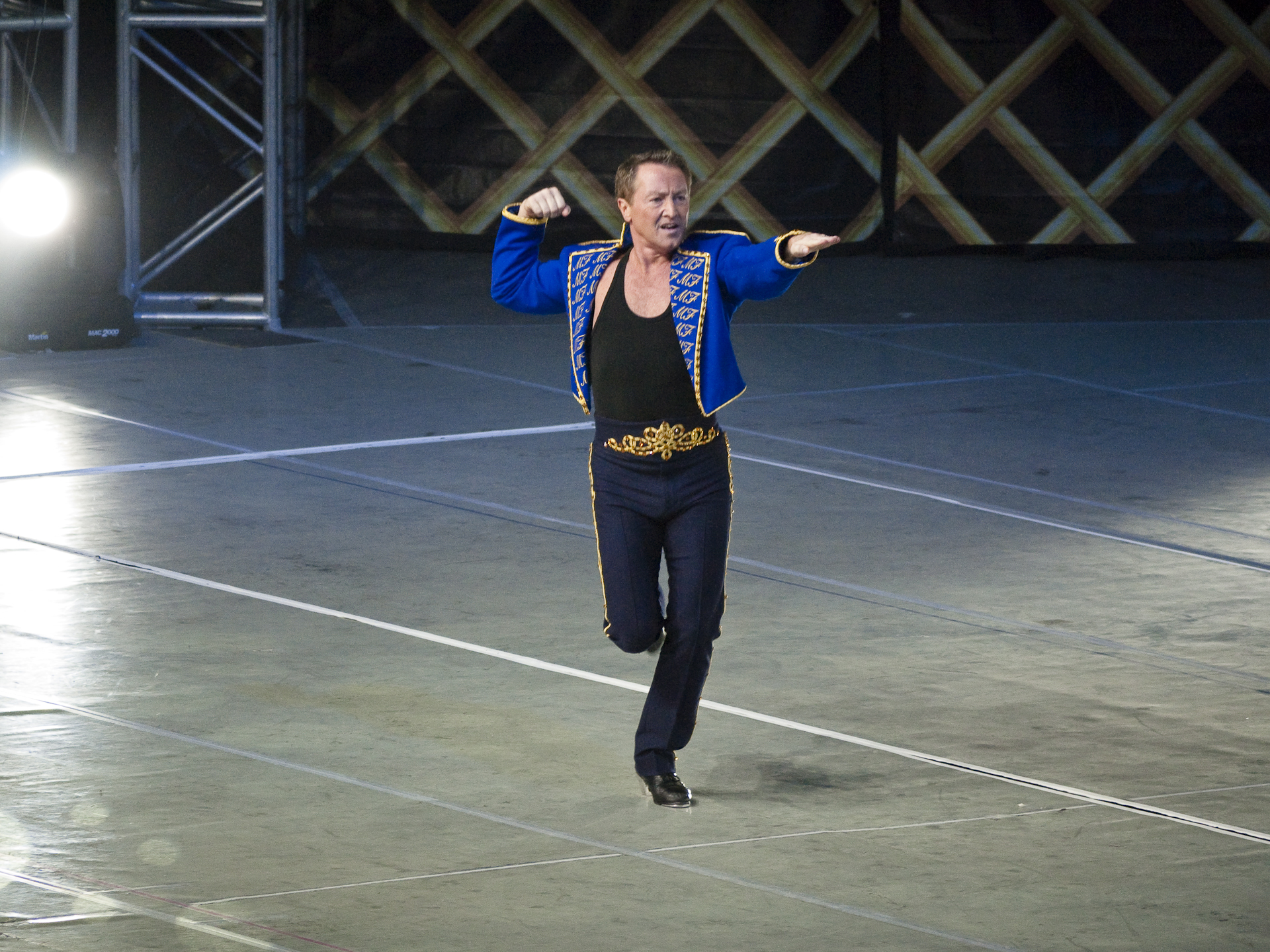 Michael Flatley dancing solo in a blue and black costume on a large stage