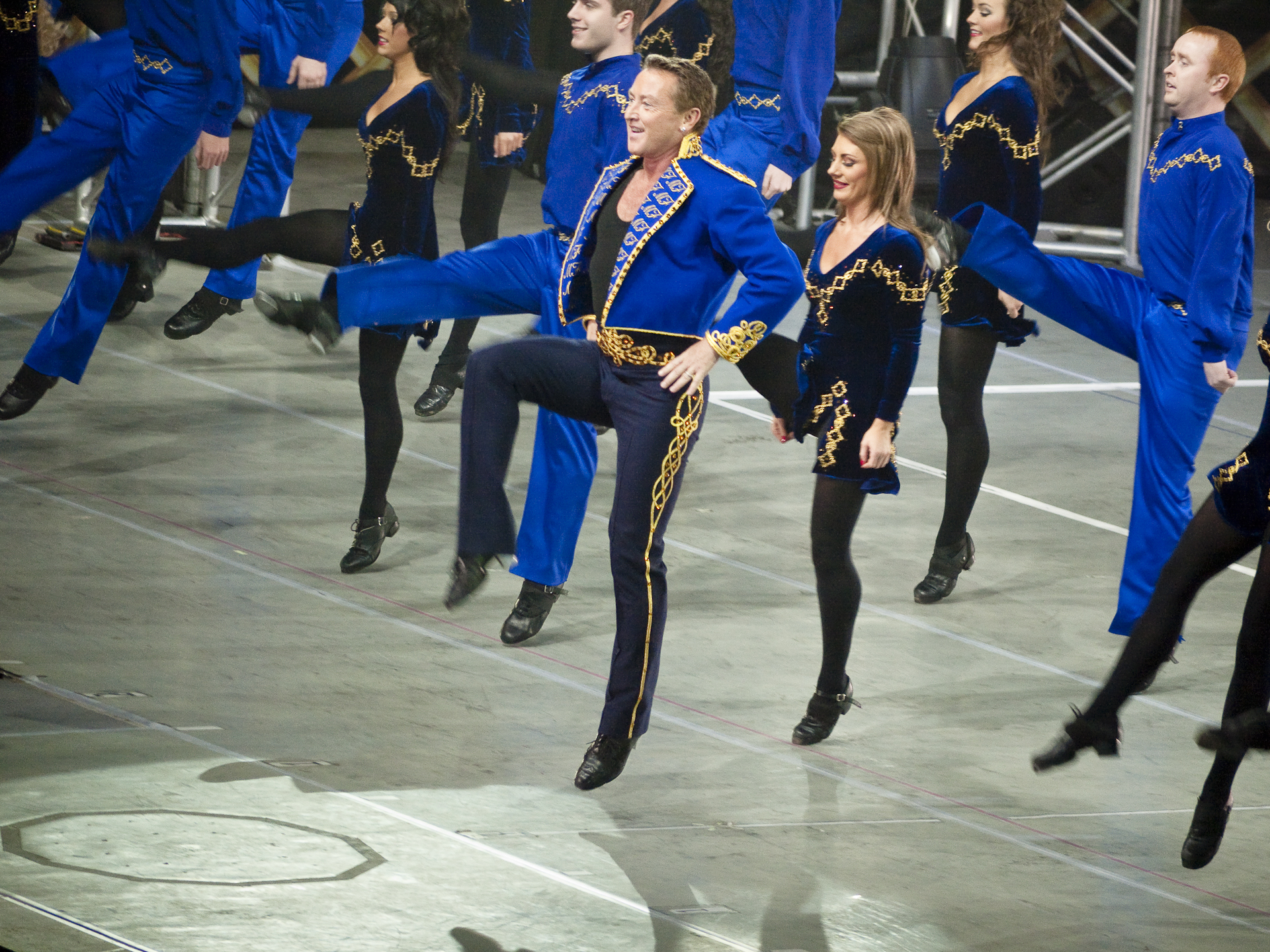 Michael Flatley and ensemble dancers performing high kicks in blue and black costumes
