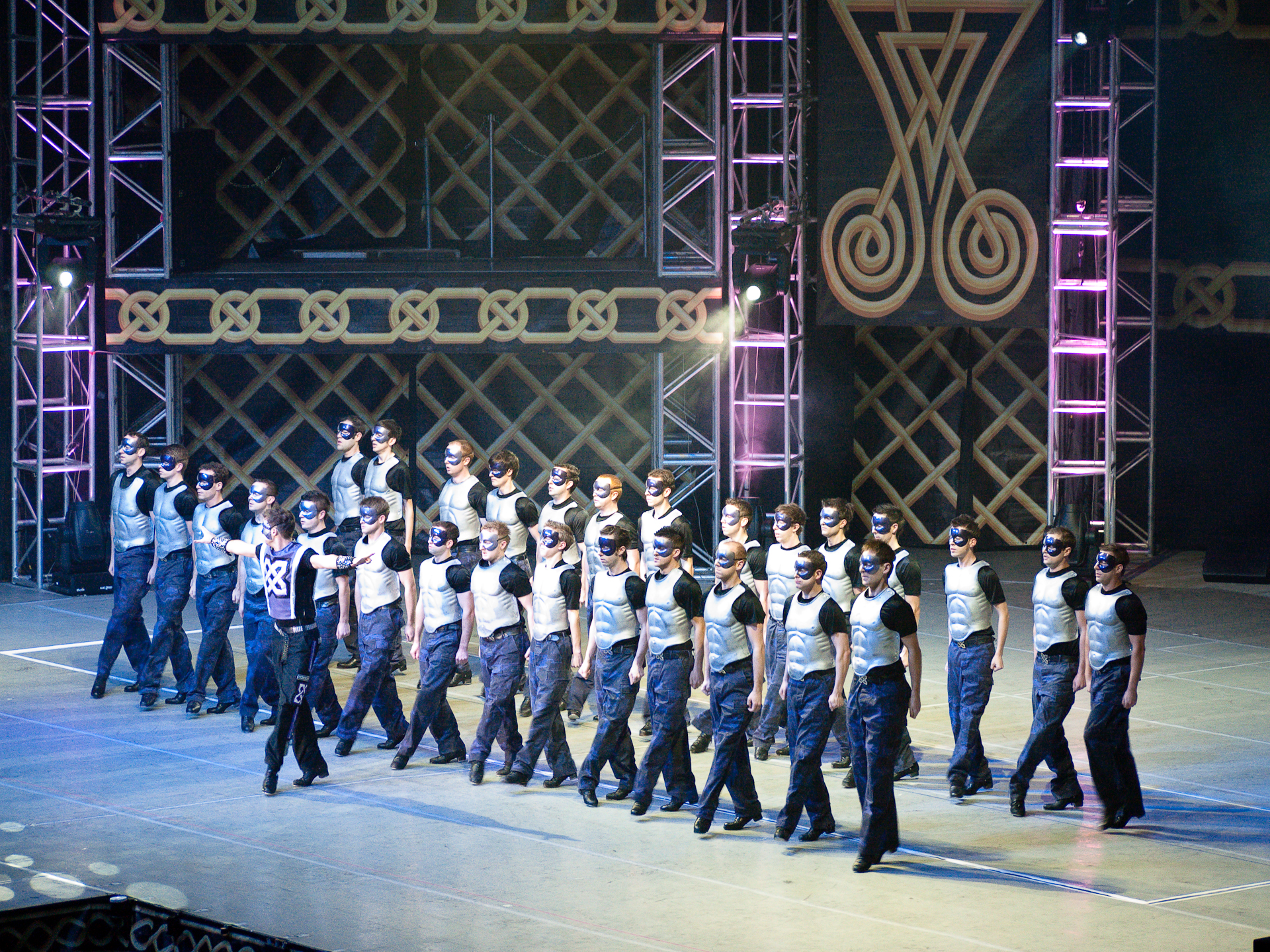 Male ensemble dancers in a synchronized line during the Warriors scene from Feet of Flames