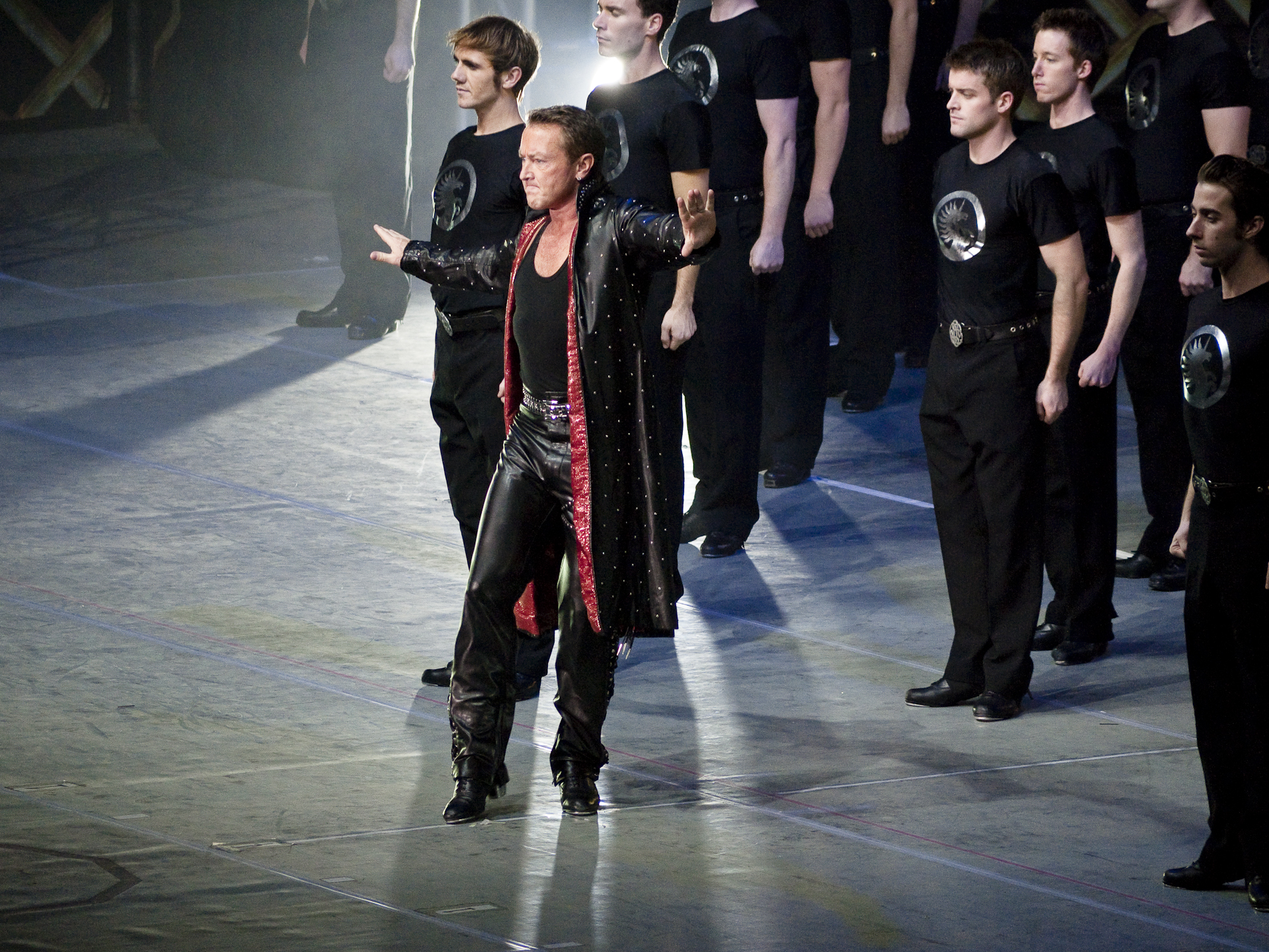 Michael Flatley onstage in a black and red costume with ensemble dancers behind him