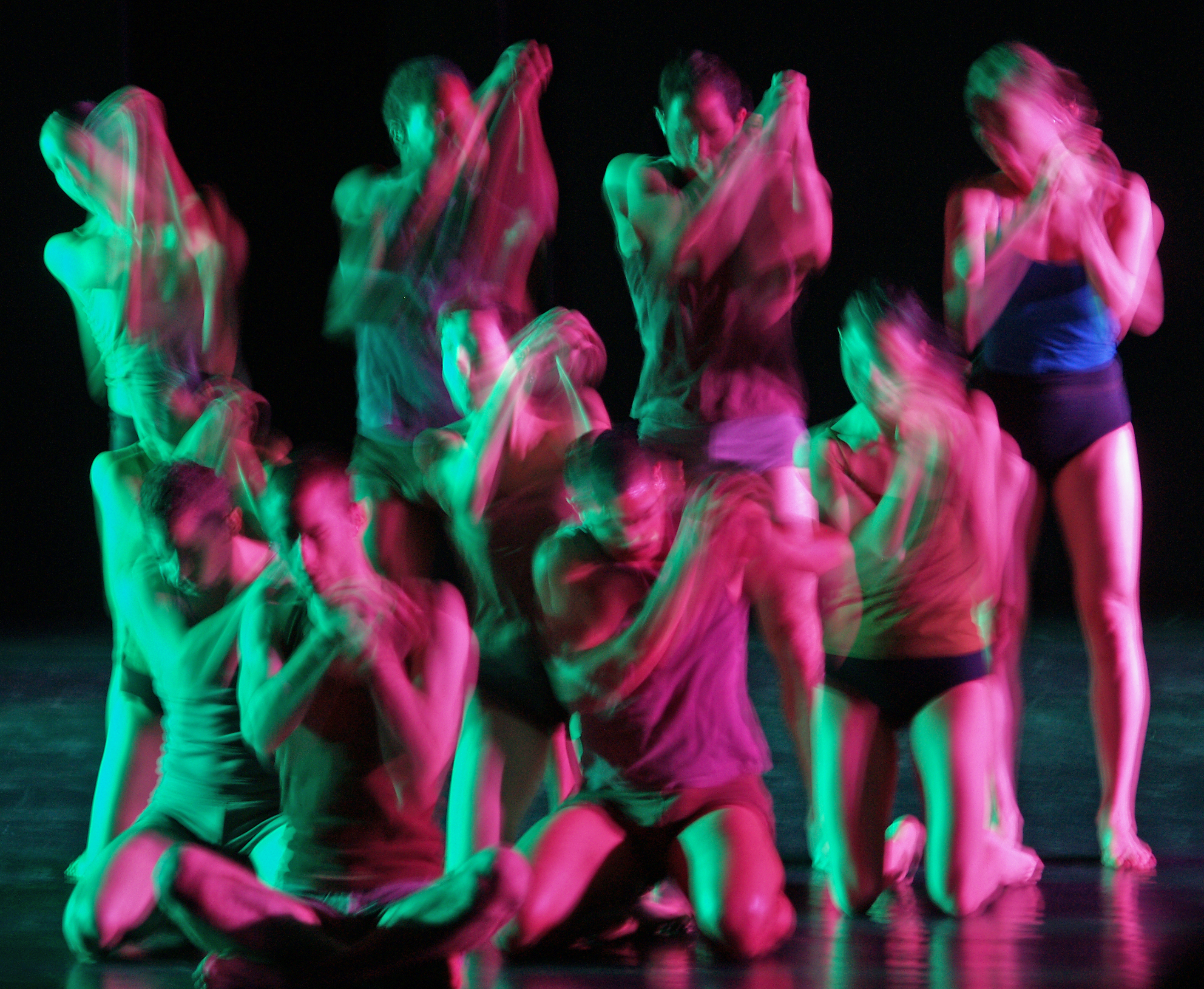 Batsheva Dance Company performers moving together under green and magenta stage lighting.
