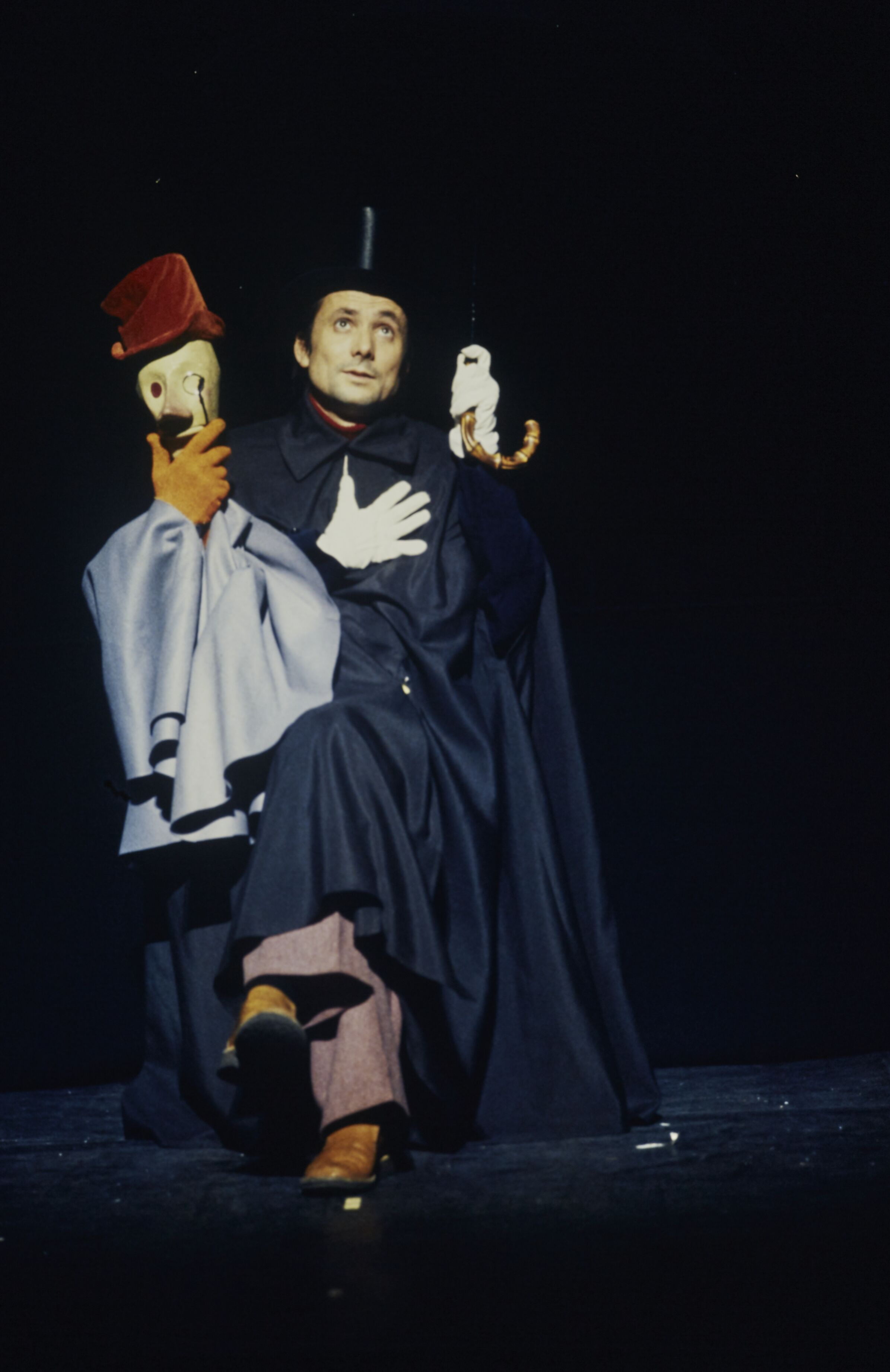 Philippe Genty seated on a dark stage beside a puppet figure during a 1977 company performance