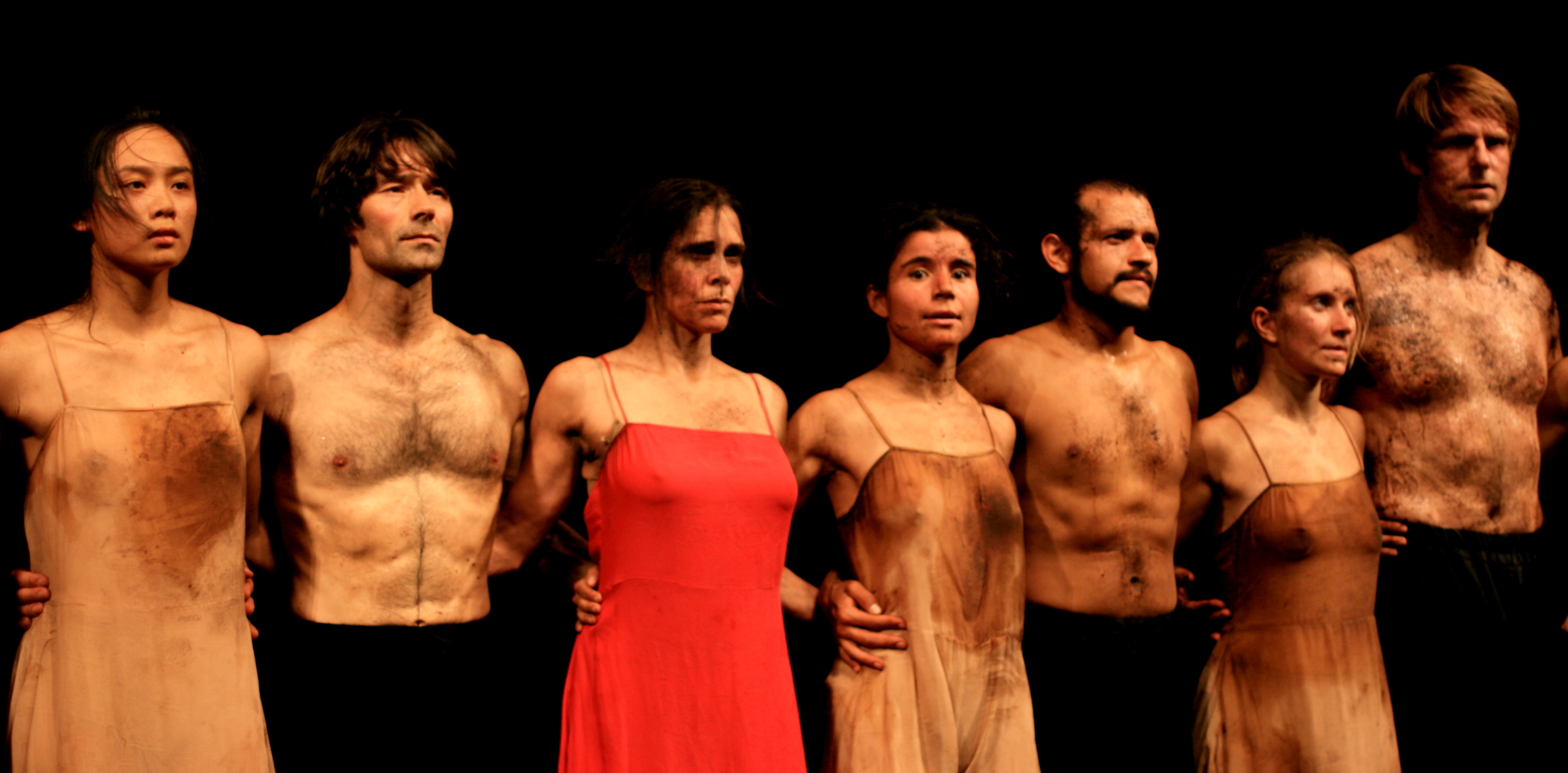 Dancers in Pina Bausch's The Rite of Spring stand together after a performance, their costumes and bodies marked by peat