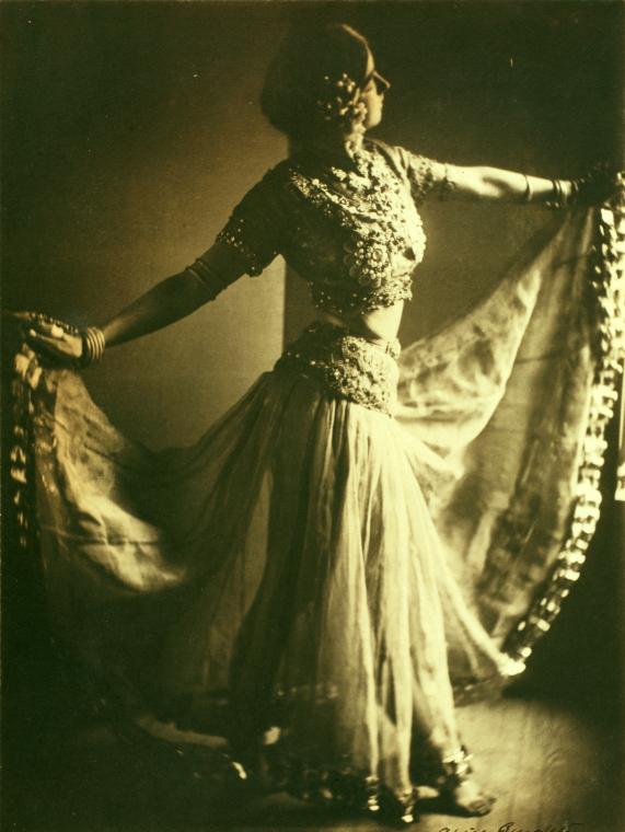 Ruth St. Denis poses with draped fabric in an atmospheric studio photograph around 1900.